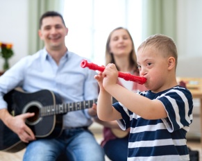 Cheerful down syndrome boy with parents playing musical recroder instrument, laughing.