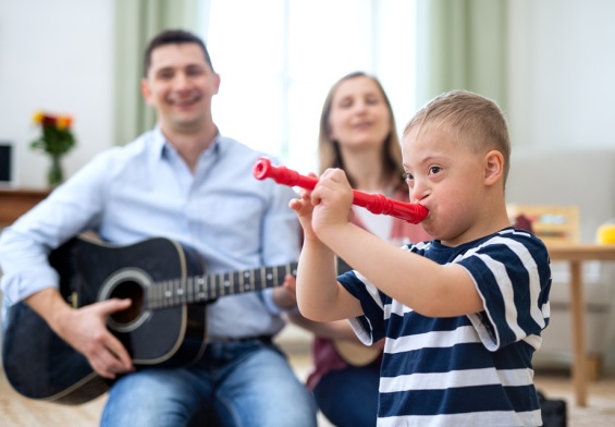 Cheerful down syndrome boy with parents playing musical recroder instrument, laughing.