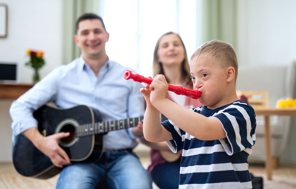 Cheerful down syndrome boy with parents playing musical recroder instrument, laughing.